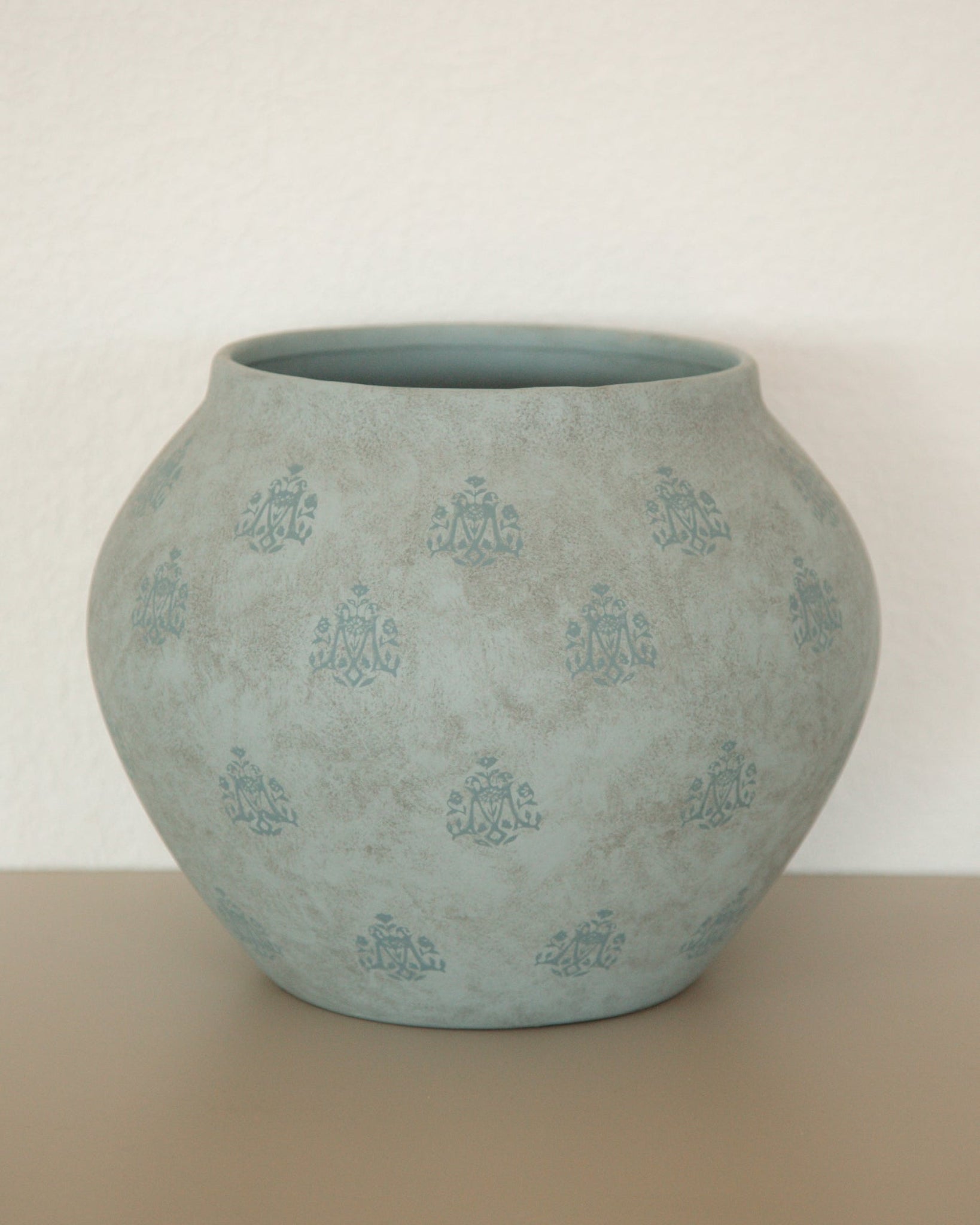 A round, bulb-shaped ceramic planter pot in a textured light blue-green glaze with a repeating embossed floral pattern, set against a neutral beige background.