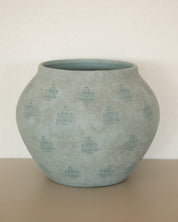 A round, bulb-shaped ceramic planter pot in a textured light blue-green glaze with a repeating embossed floral pattern, set against a neutral beige background.