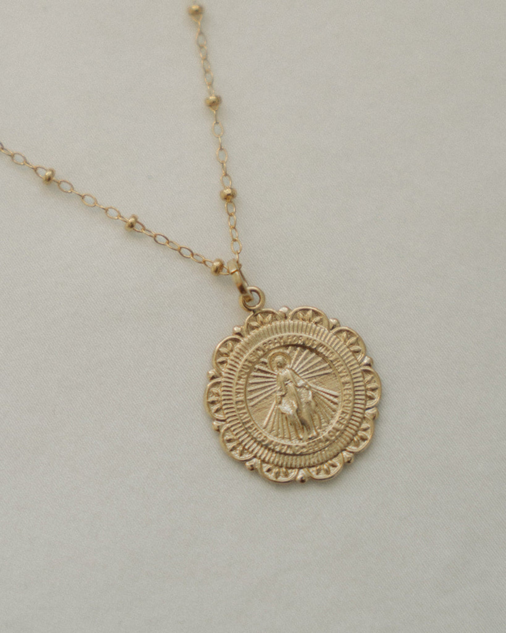 Gold miraculous medal necklace on a light gray background