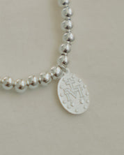 Silver beaded bracelet with the Marian symbol on a beige background