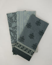 Three folded cotton towels in muted blue-green tones with floral and striped patterns, arranged on a light neutral background.