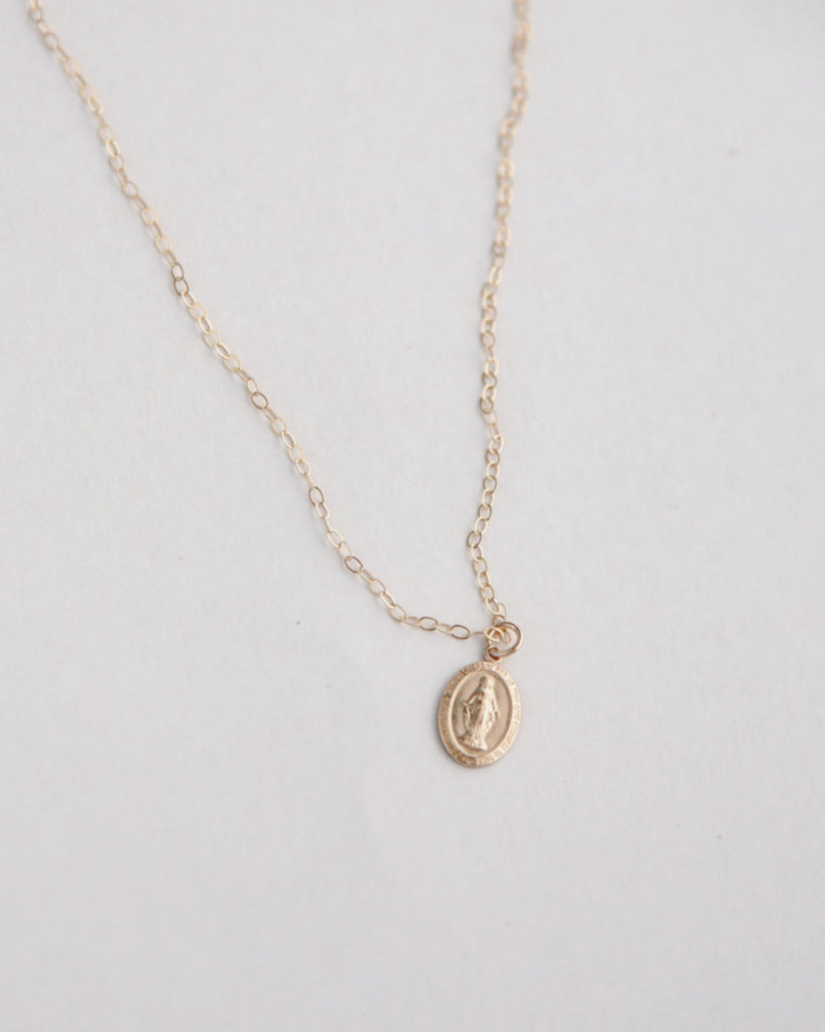 Gold miraculous medal necklace on a light gray background