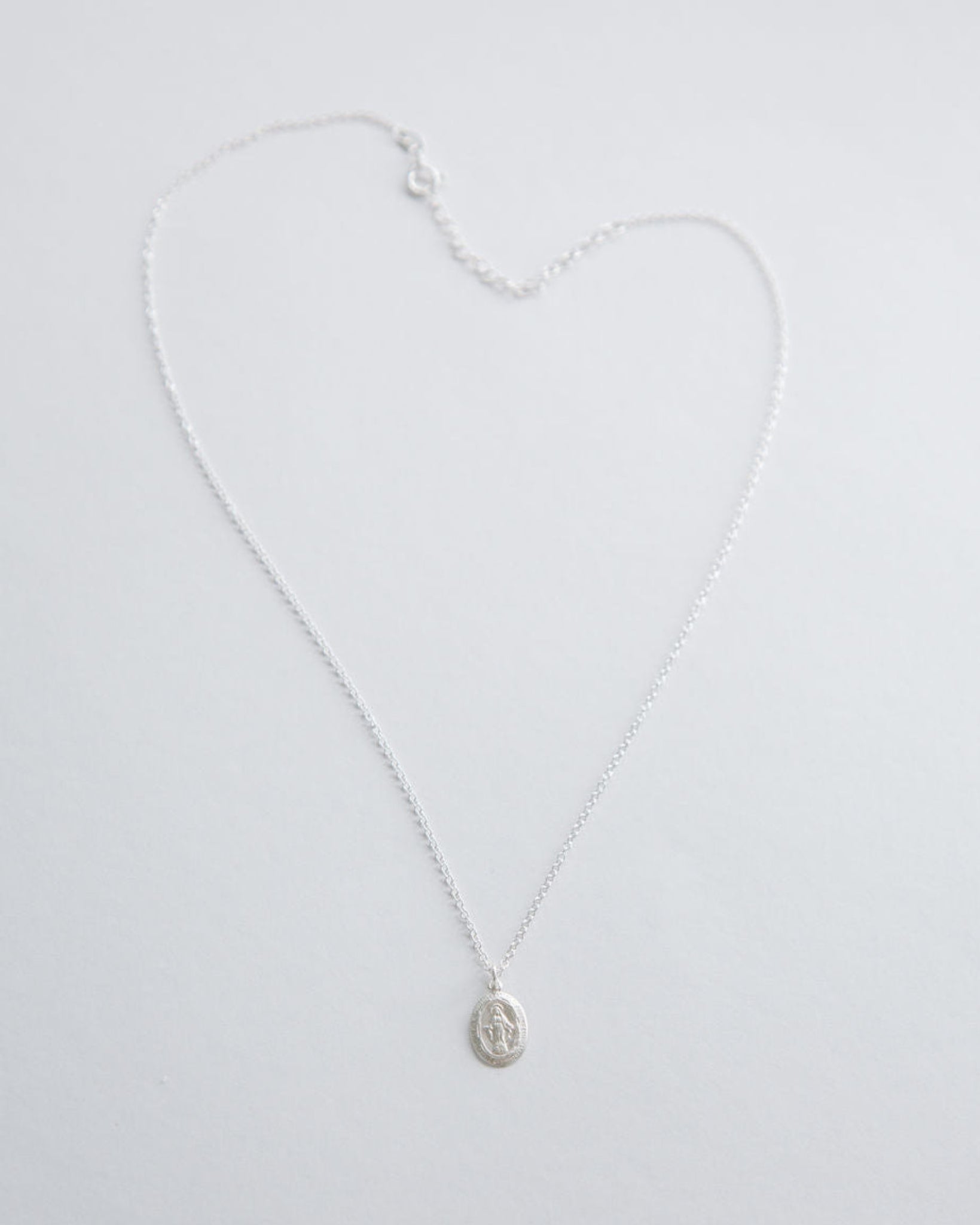 Silver miraculous medal necklace on a light gray background
