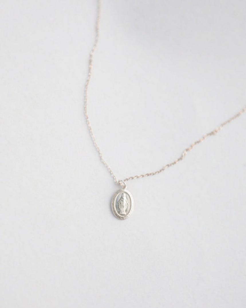 Silver miraculous medal mary necklace on a light gray background