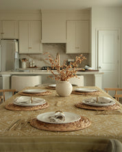 A modern kitchen with a styled table setting — beautiful place settings arranged on the Cana Tablecloth by West Coast Catholic, a mustard-yellow cloth featuring the Chi-Rho and other Catholic symbols.