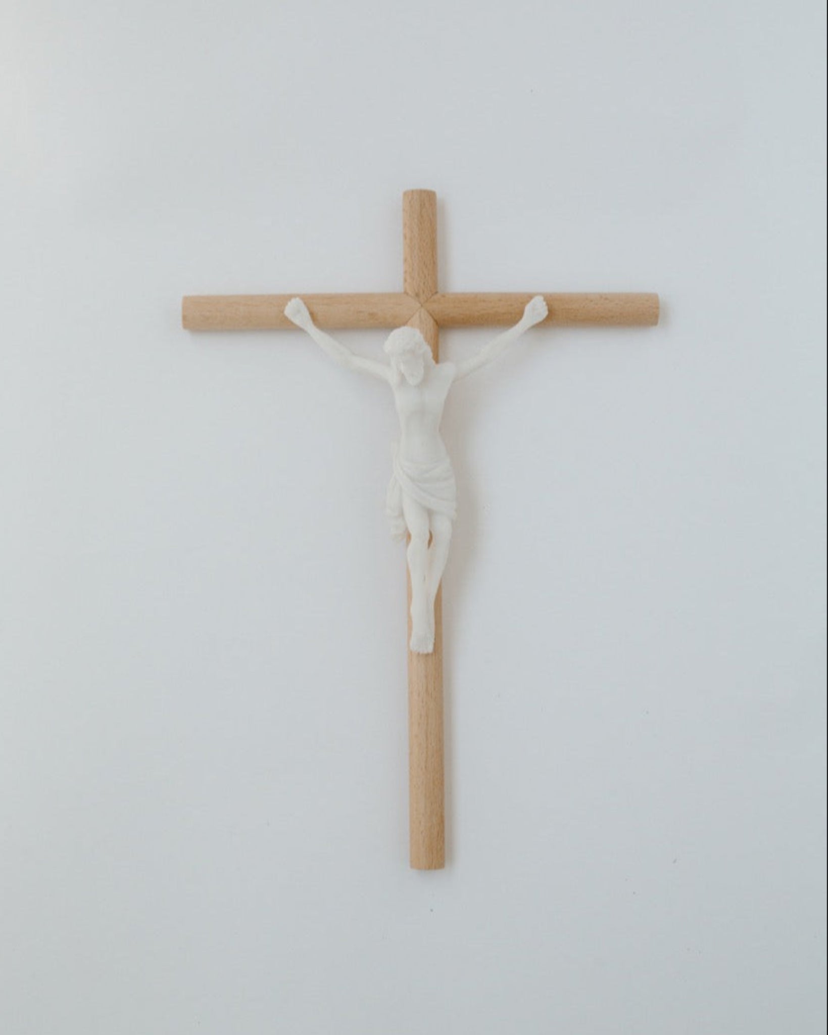 A wall-mounted crucifix with a modern, minimalistic aesthetic, featuring a wooden cross and a white figure of Jesus Christ.