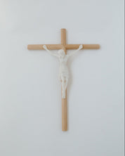 A wall-mounted crucifix with a modern, minimalistic aesthetic, featuring a wooden cross and a white figure of Jesus Christ.