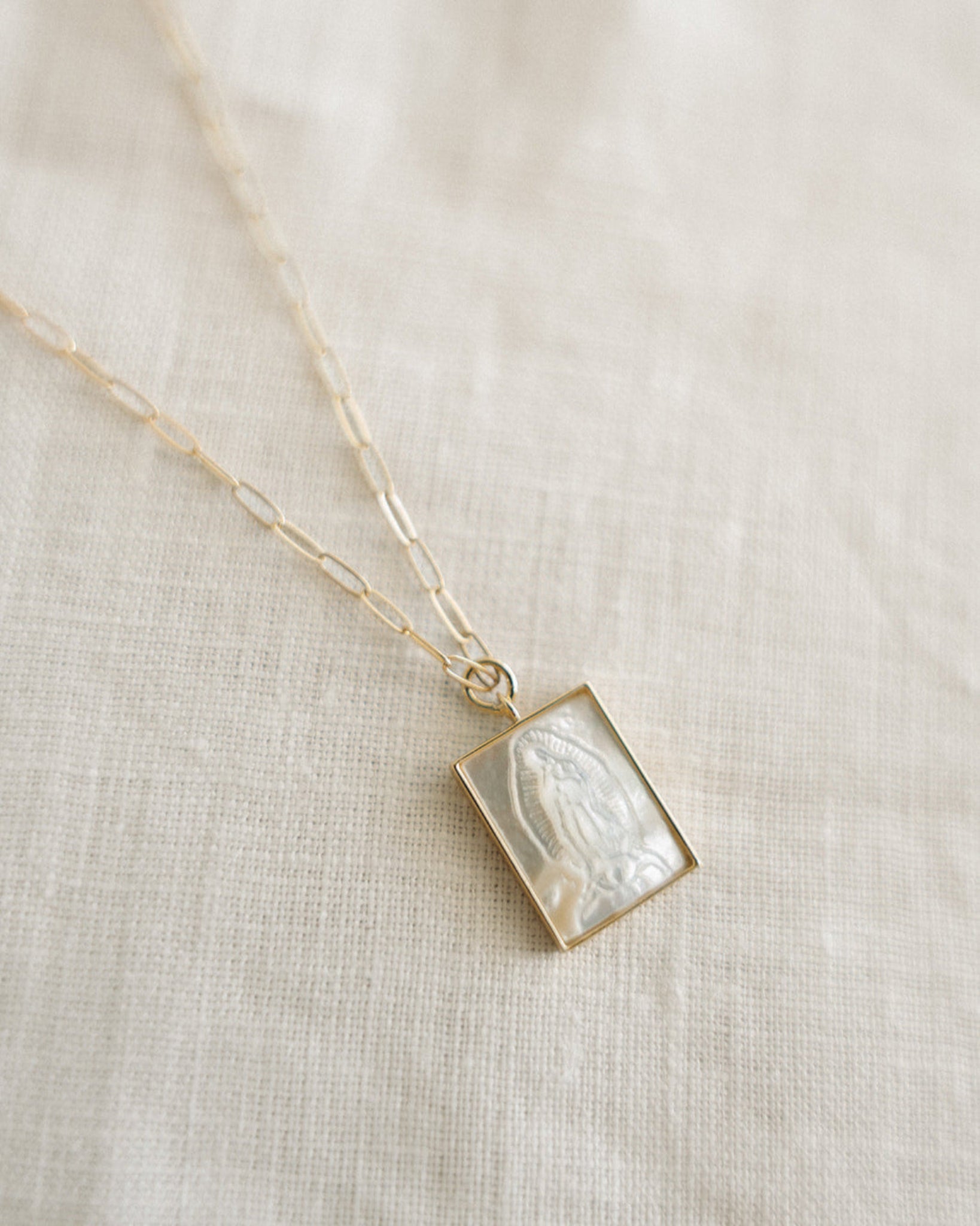 Necklace with a pearl our Lady of Guadalupe design on a beige fabric background