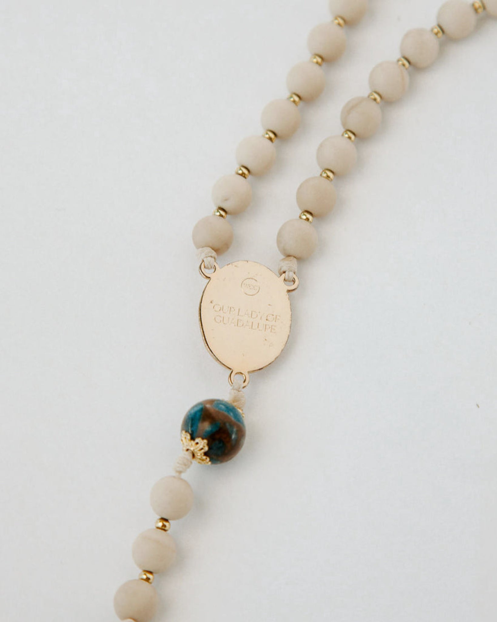 Beaded necklace with a gold tag and a blue and green bead on a white background
