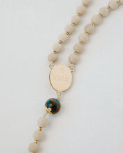 Beaded necklace with a gold tag and a blue and green bead on a white background