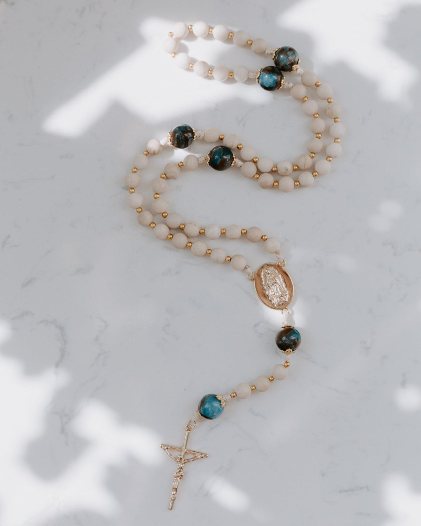 Rosary with turquoise and gold beads on a marble surface