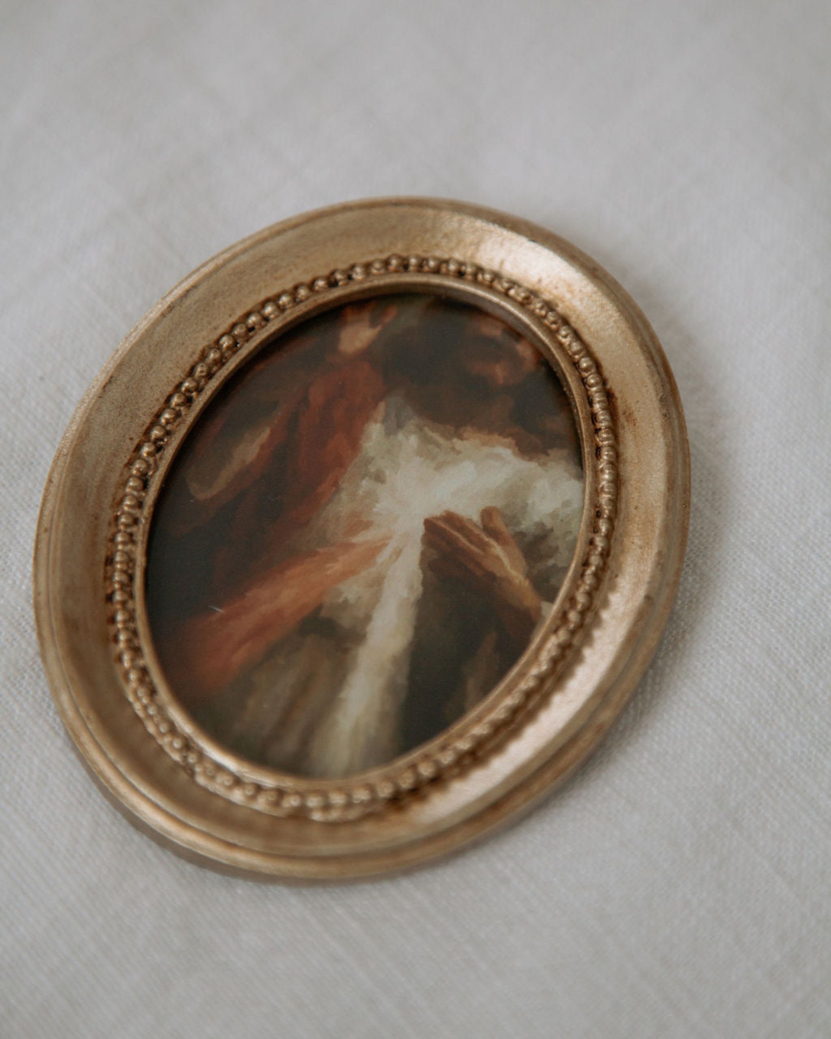 Small oval painting in a gold frame on a light gray background