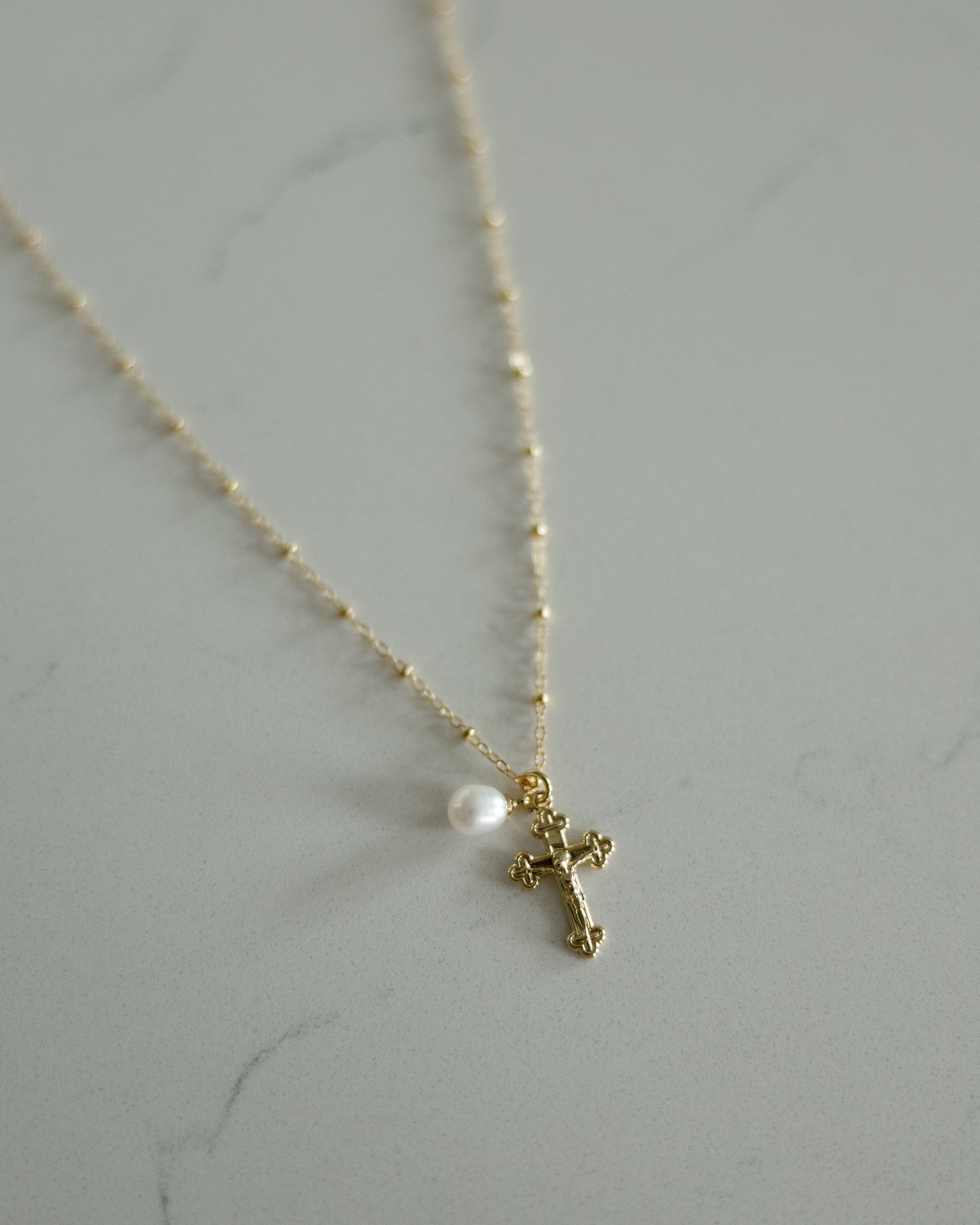 Gold crucifix necklace with a pearl on the beaded chain. 