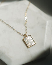 Gold pearl Guadalupe necklace with a paper clip chain on a light surface
