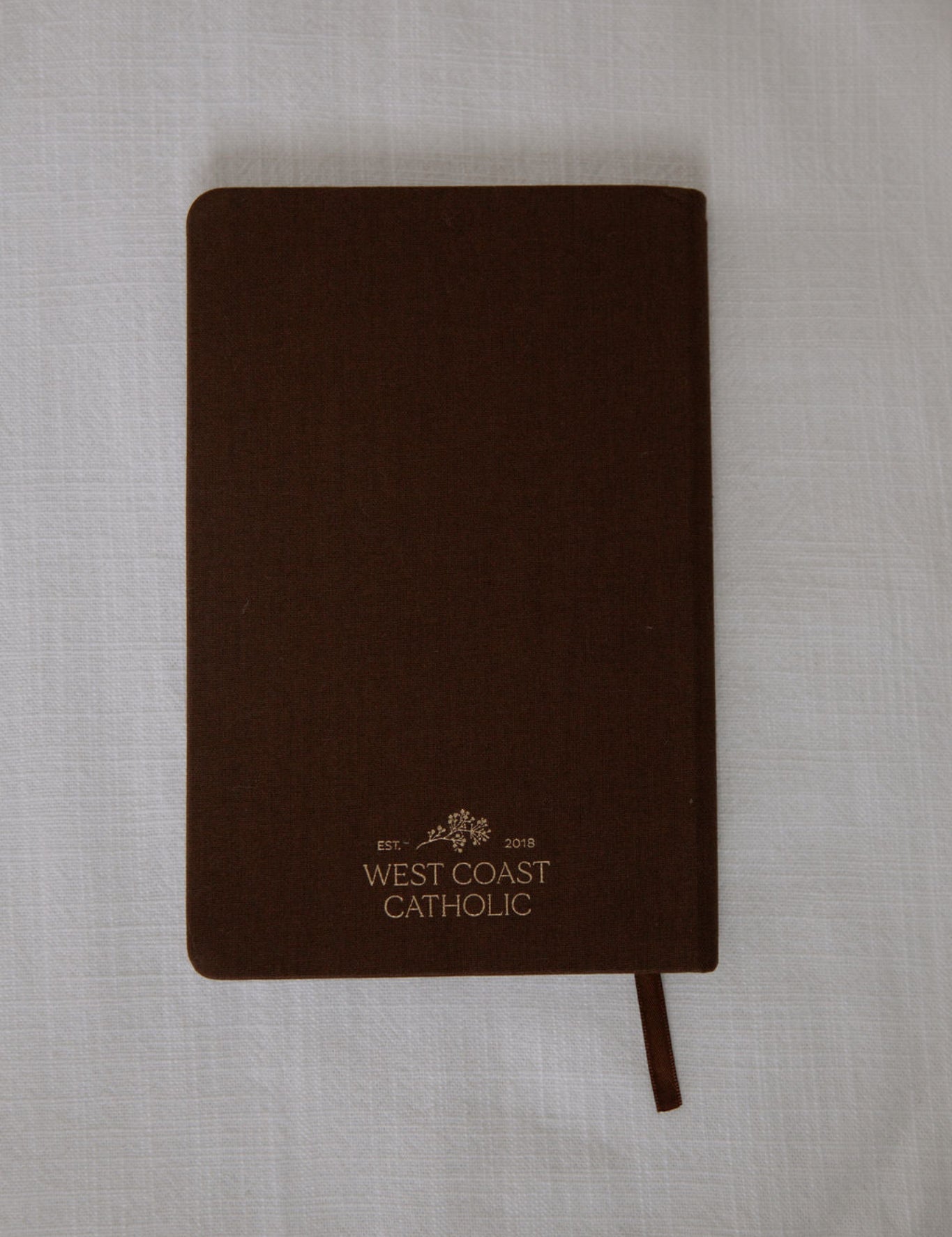Brown notebook with 'West Coast Catholic' branding on a light gray background