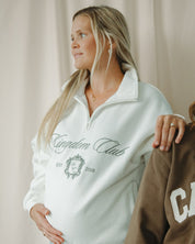 Woman wearing a white sweatshirt with 'Kingdom Club' text, standing next to another person.