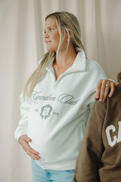 Woman wearing a white sweatshirt with 'Kingdom Club' text, standing next to another person.