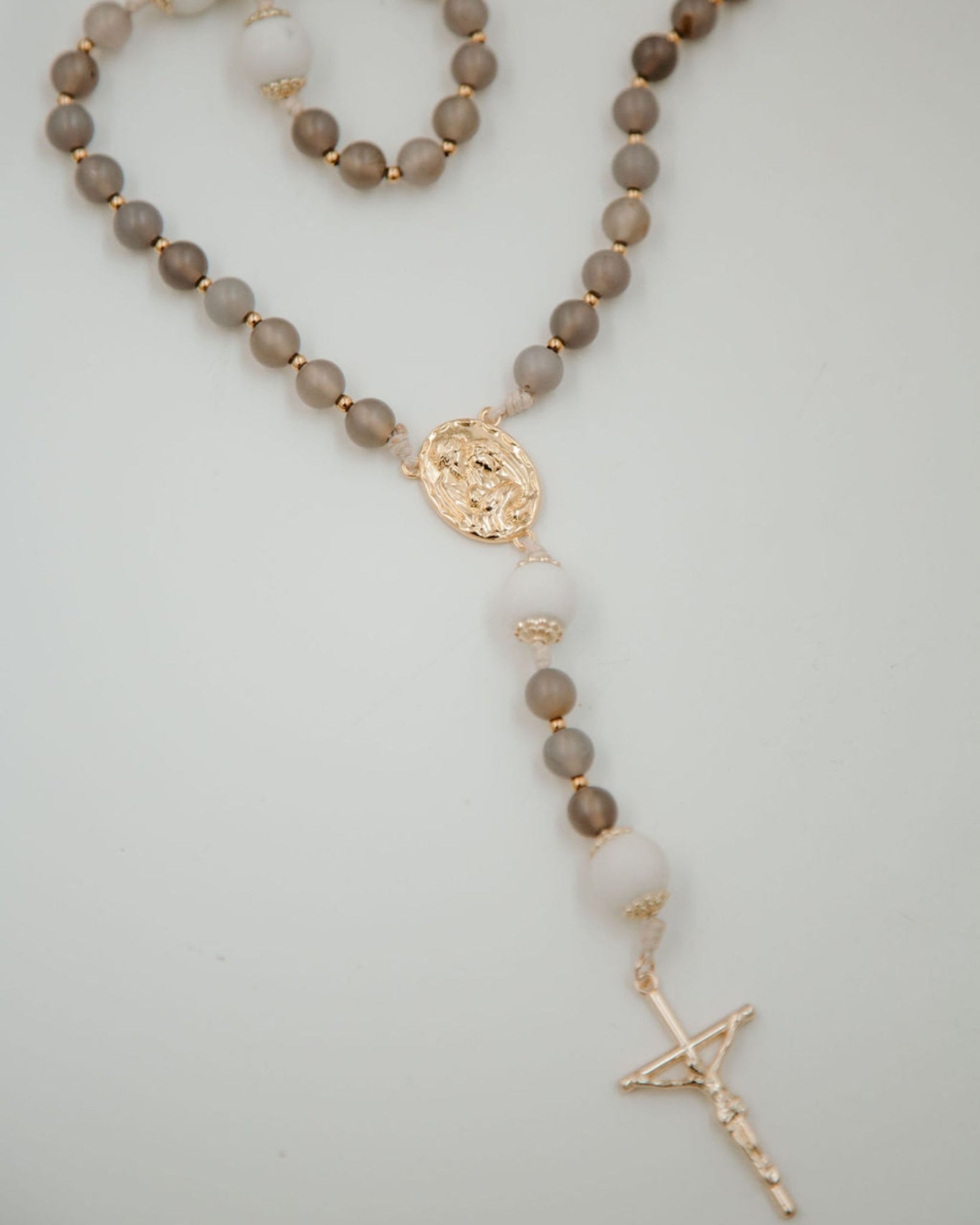 Catholic rosary with gray beads and gold accents on a light background