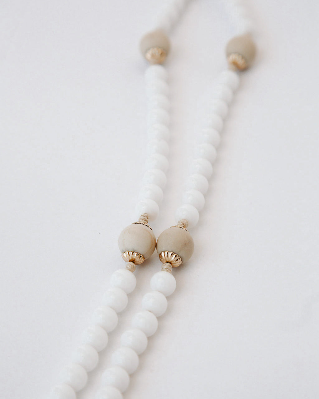 Rosary with white beads and gold accents on a light gray background