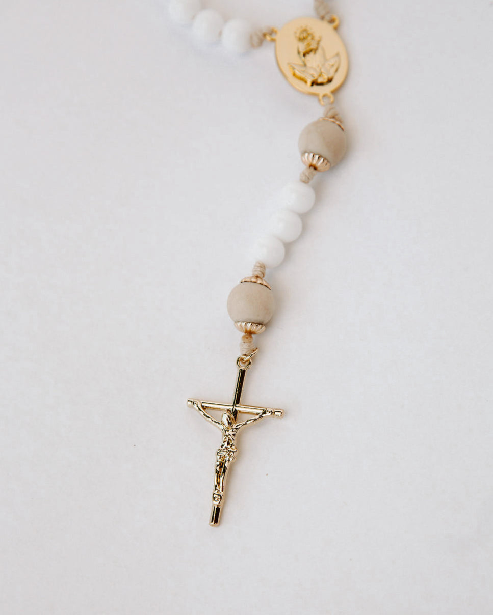 Rosary with white beads and gold Crucifix on a light gray background