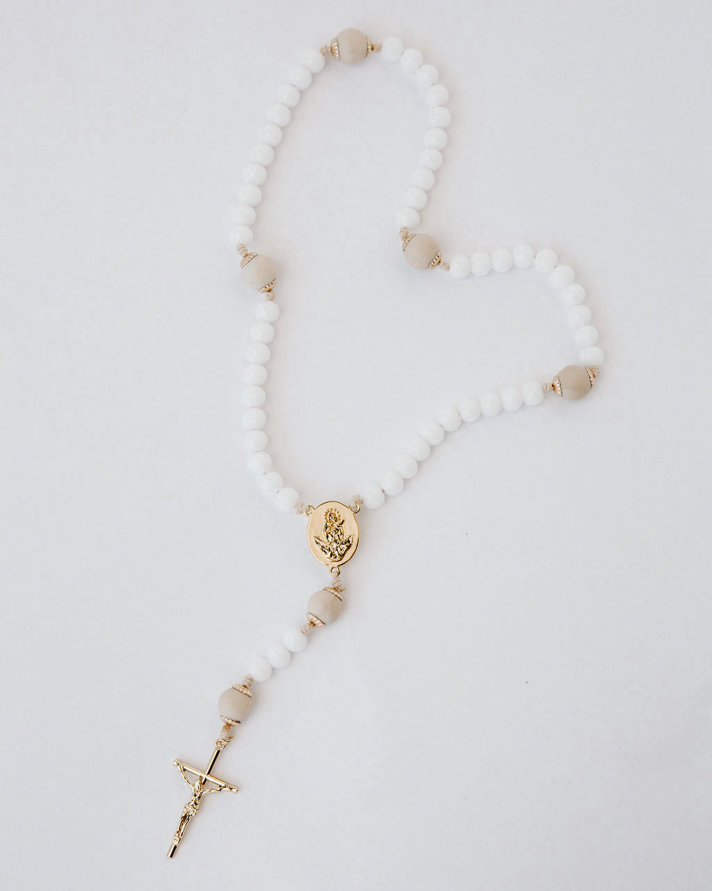 Rosary with white beads and gold accents on a light gray background
