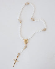 Rosary with white beads and gold accents on a light gray background