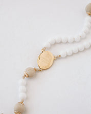 Rosary with white beads and gold accents on a light gray background
