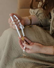 Person holding a white rosary with a neutral background