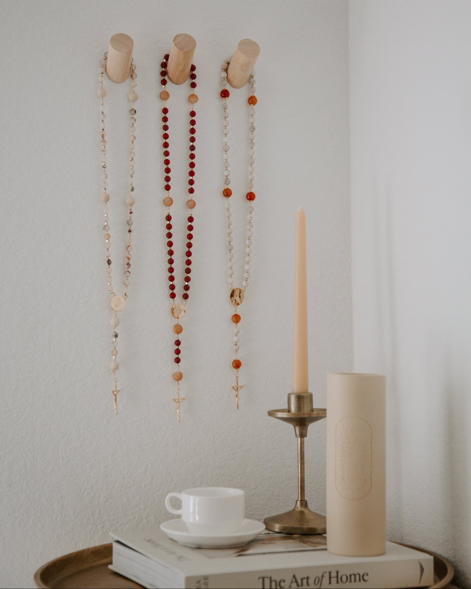 Decorative wall hooks with rosaries and a candle on a table with books and a cup.