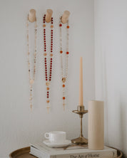 Decorative wall hooks with rosaries and a candle on a table with books and a cup.