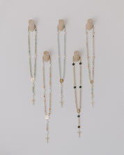 Set of five rosary pegs with rosaries of various bead designs on a light gray background
