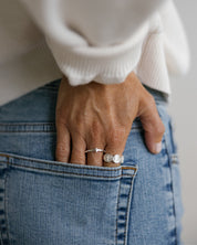 A close-up lifestyle shot of a person wearing silver catholic rings with a white ribbed sweater and blue jeans, looking over their shoulder.