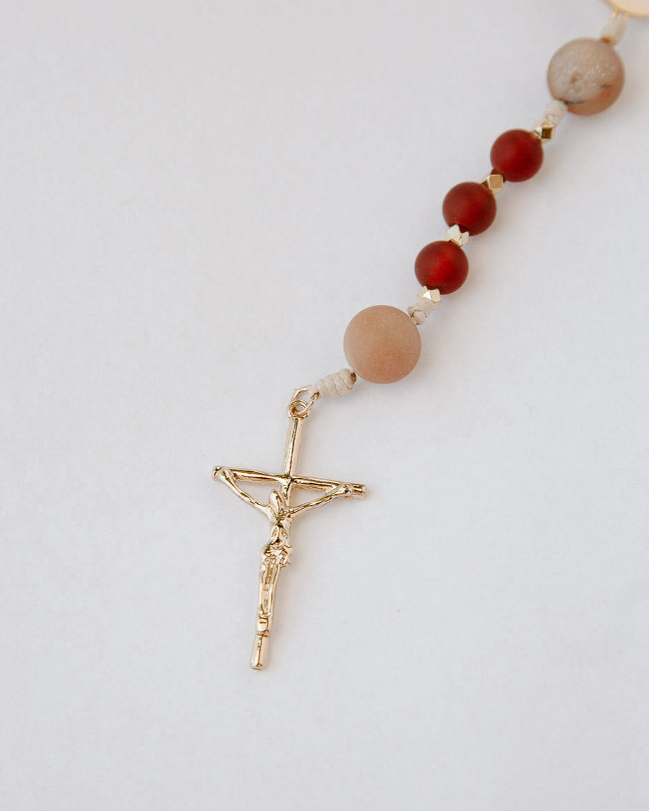 Rosary with brown and red beads and a gold cross on a light gray background