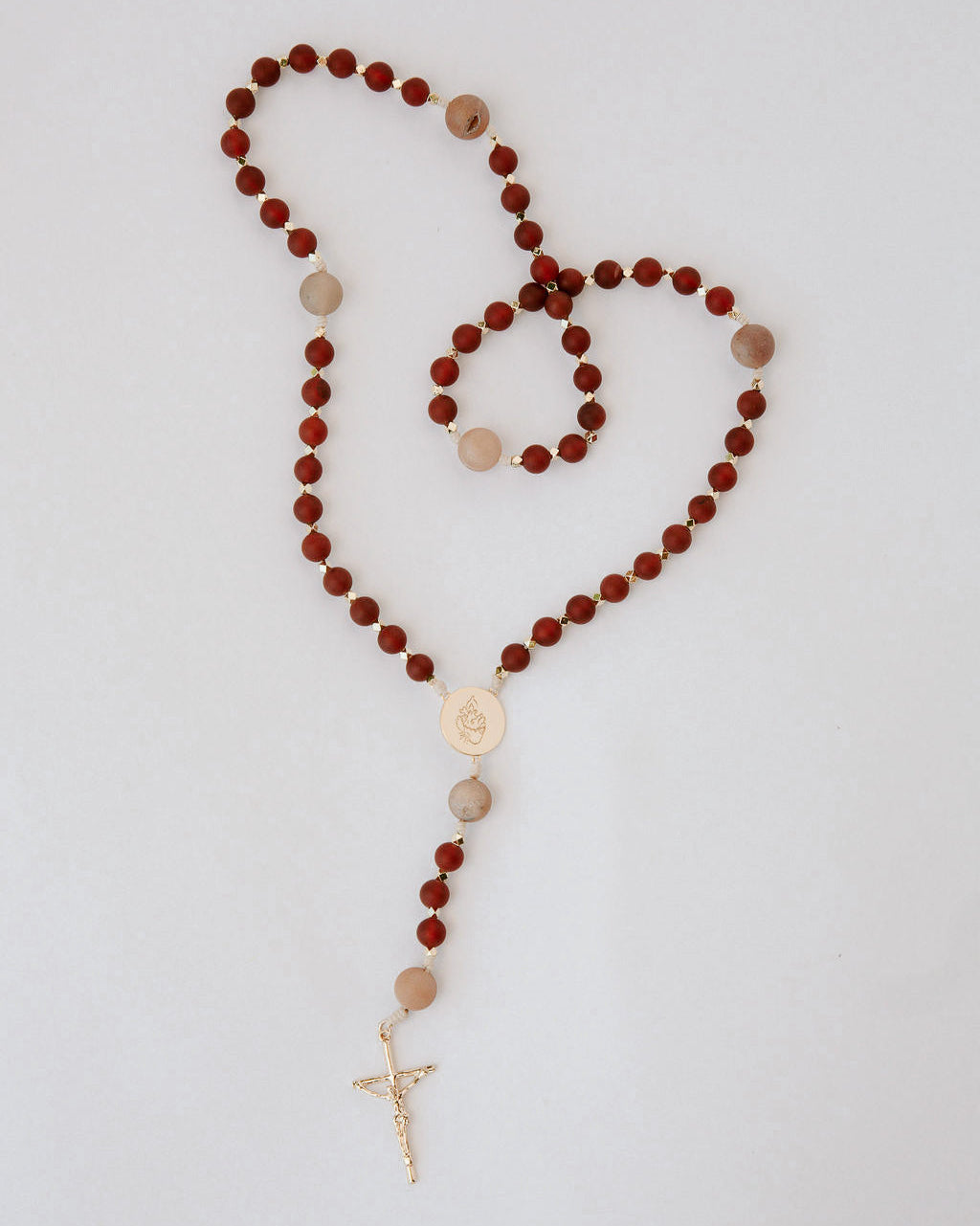 Rosary with red and beige beads and a gold cross on a light gray background