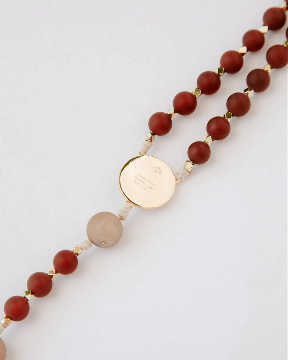 Beaded rosary with a gold medal on a light gray background