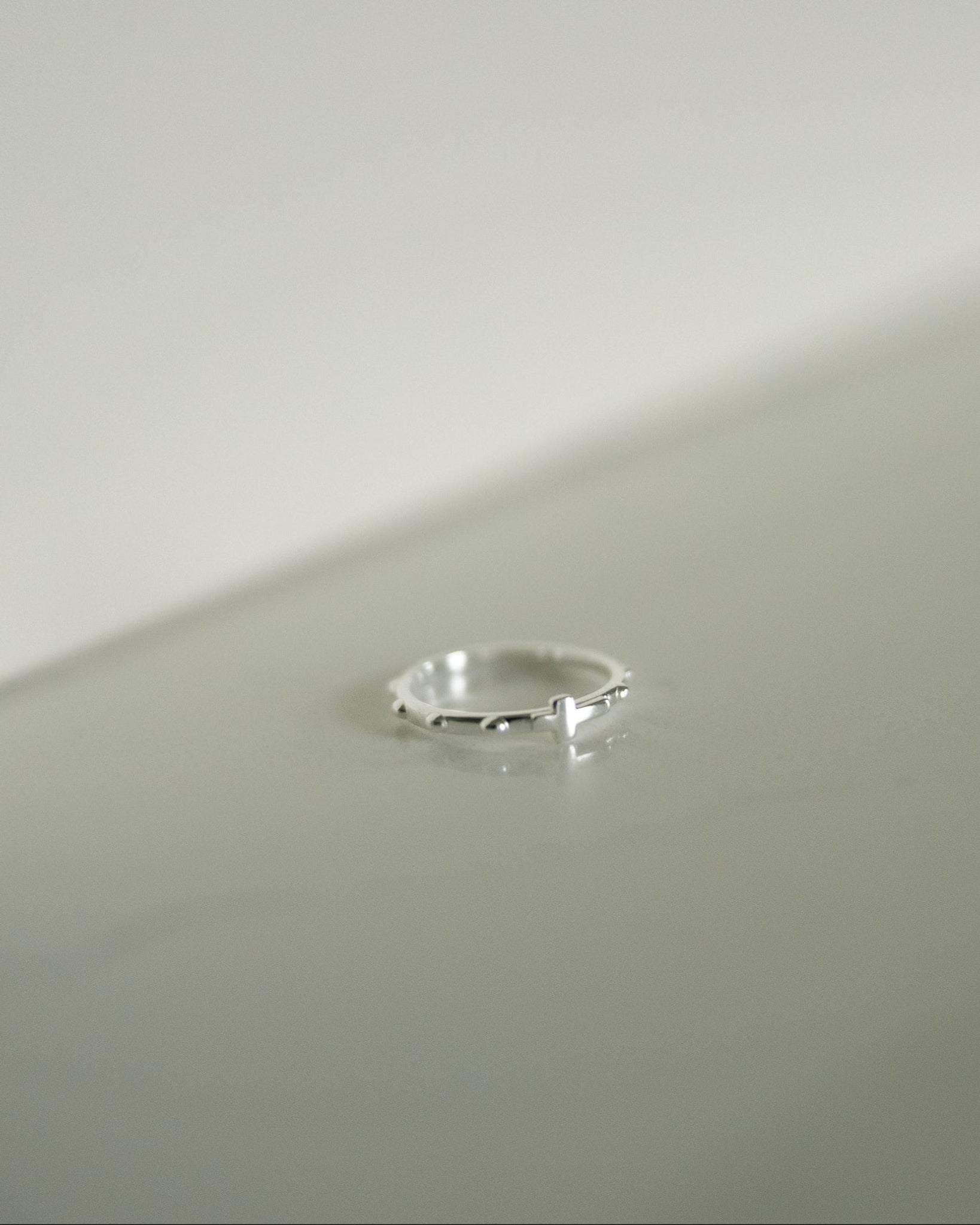 A delicate silver rosary ring resting on a minimalist light gray surface.