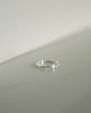 A delicate silver rosary ring resting on a minimalist light gray surface.