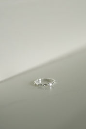 A delicate silver rosary ring resting on a minimalist light gray surface.