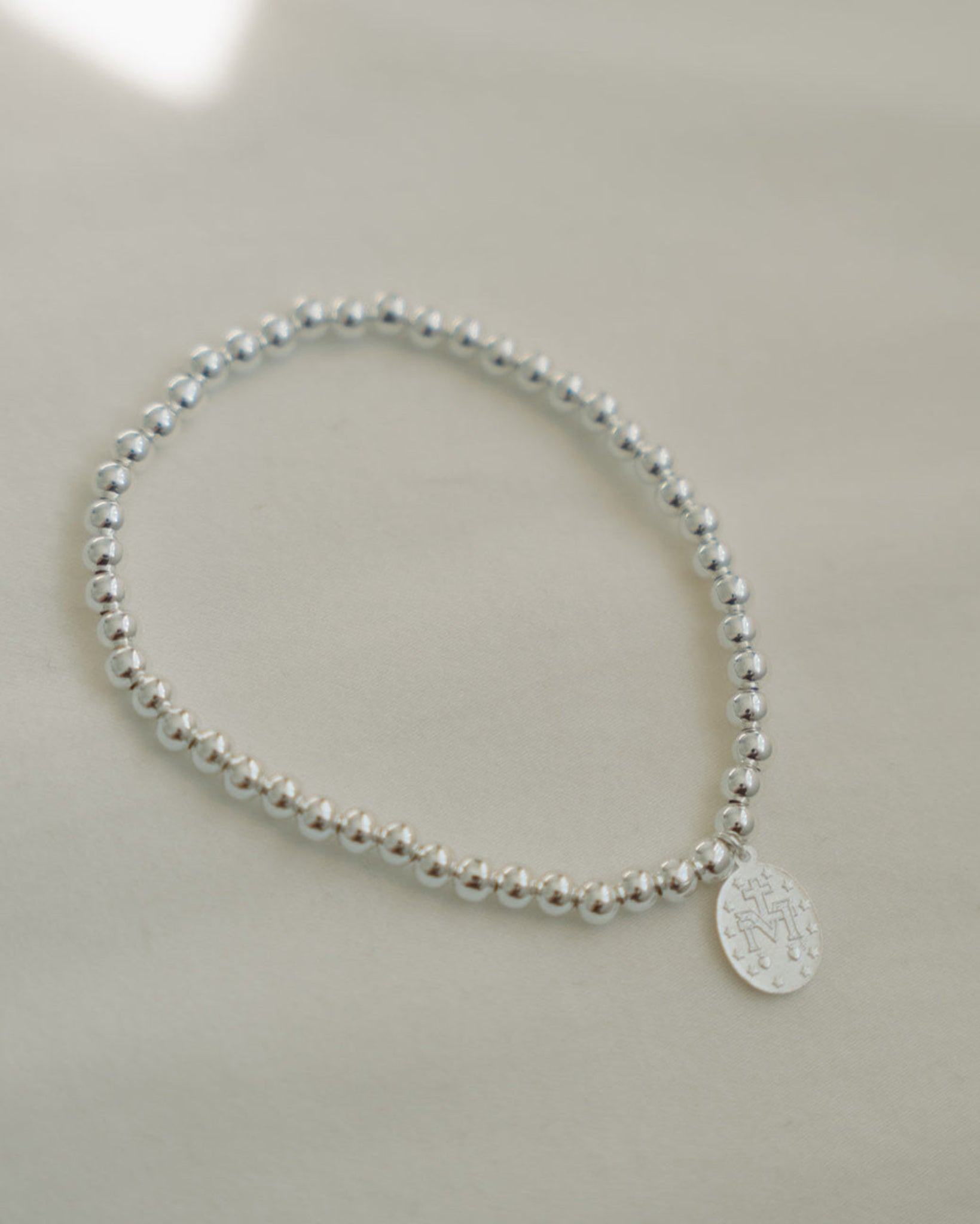 Silver beaded bracelet with a miraculous medal on a light gray background