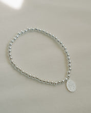 Silver beaded bracelet with a miraculous medal on a light gray background