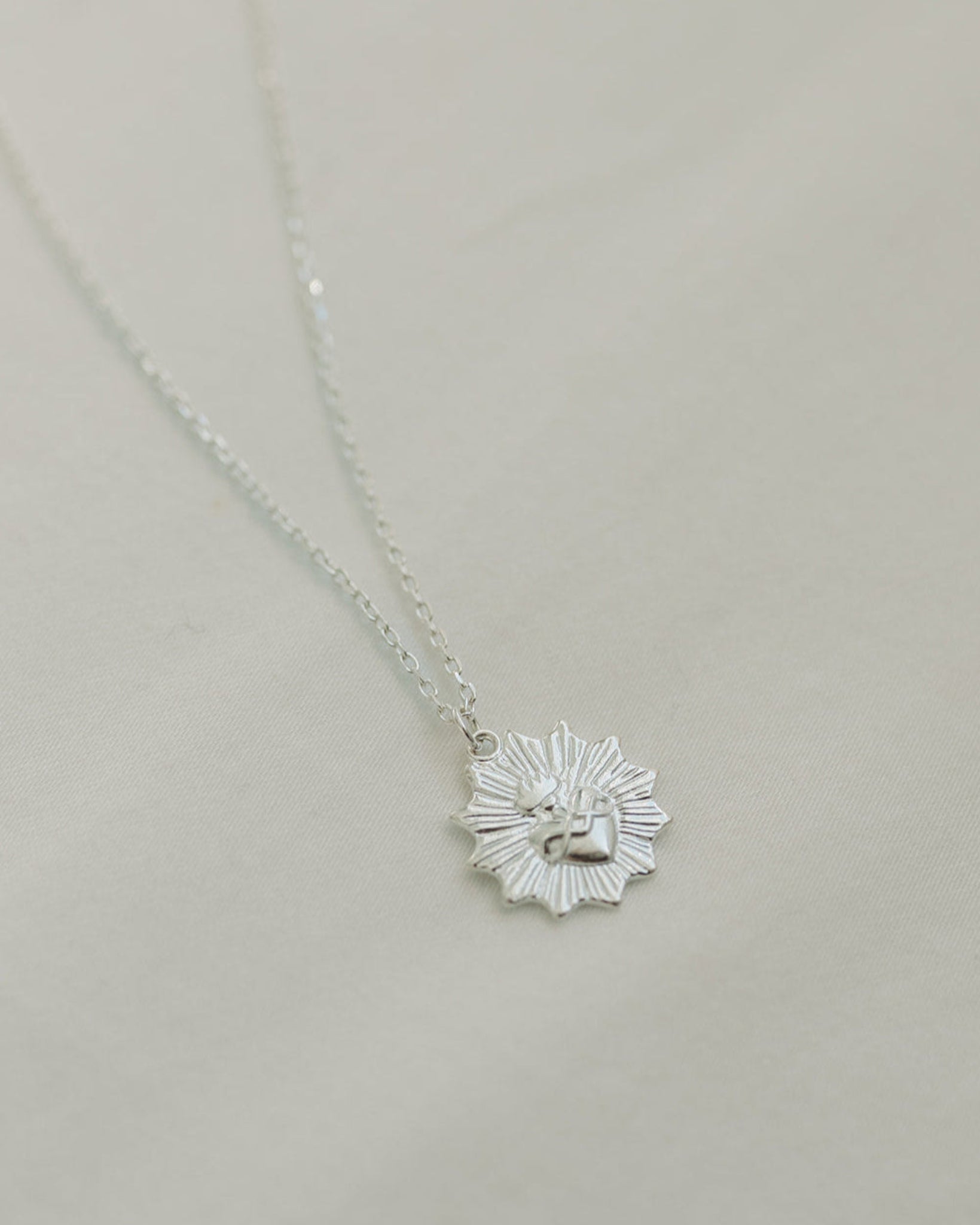 Silver necklace with a sacred heart pendant on a light gray background