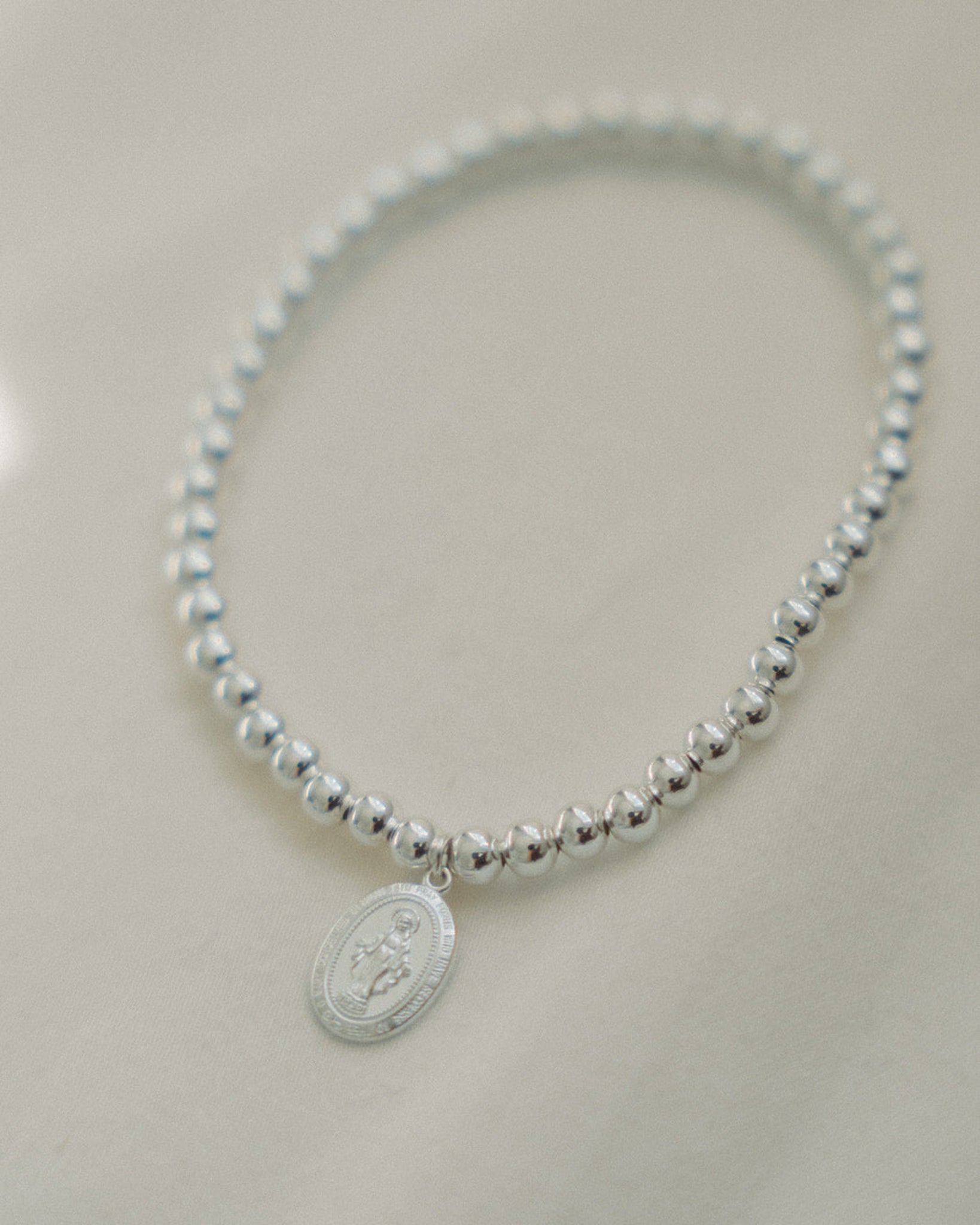 Silver beaded bracelet with a miraculous medal on a light gray background