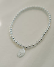 Silver beaded bracelet with a miraculous medal on a light gray background