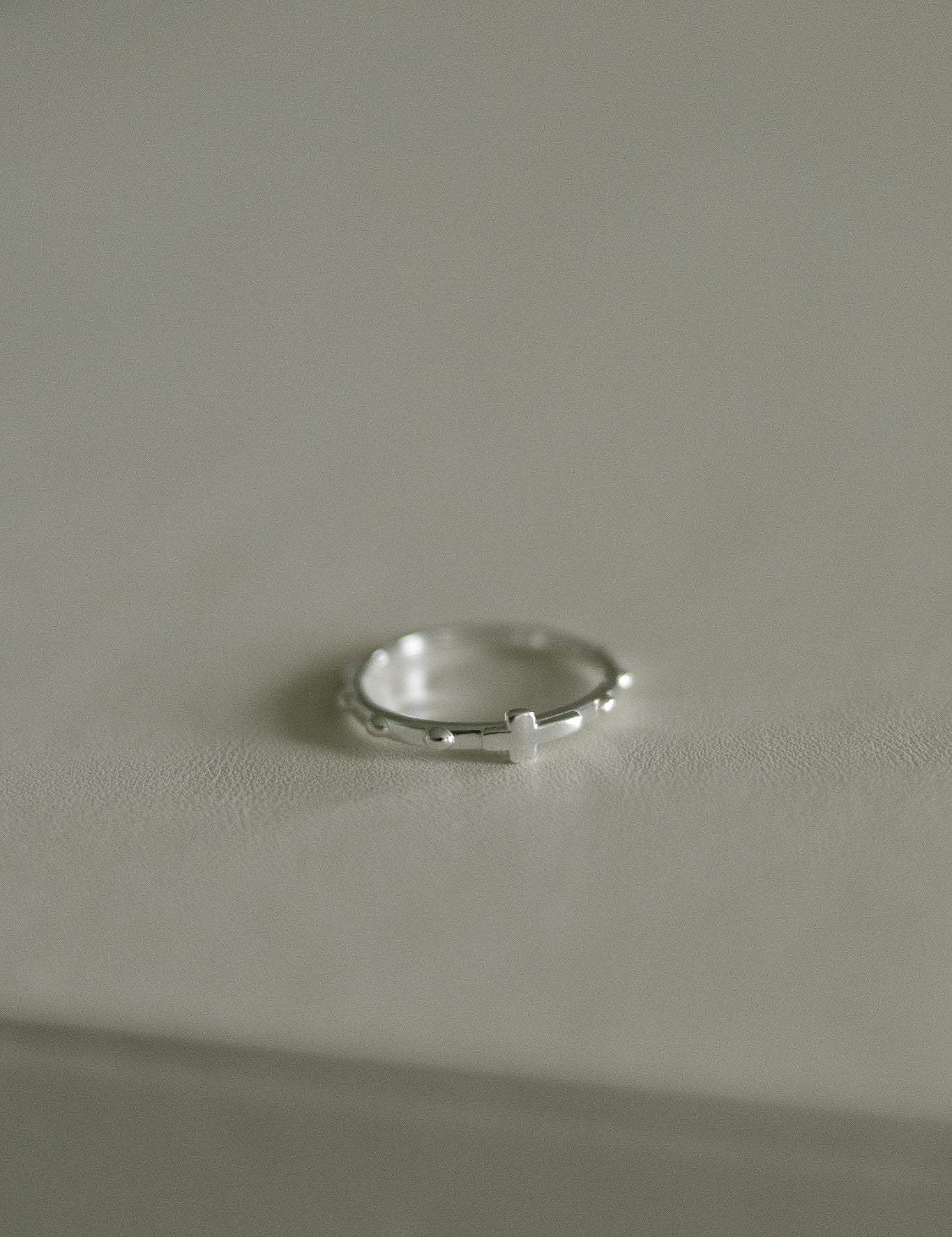 A delicate silver rosary ring resting on a neutral light gray surface.