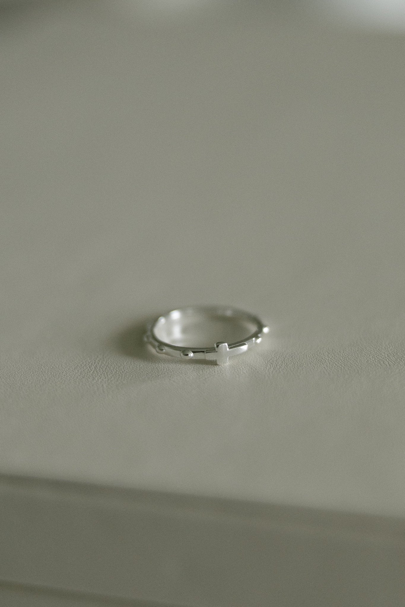 A delicate silver rosary ring resting on a neutral light gray surface.