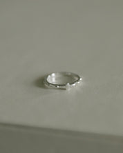A delicate silver rosary ring resting on a neutral light gray surface.