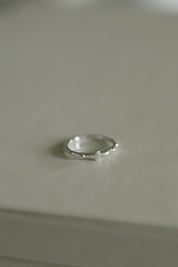 A delicate silver rosary ring resting on a neutral light gray surface.