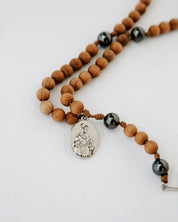 Beaded rosary with wooden beads, black beads, and a silver pendant on a white background