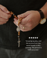 Person holding a wooden rosary with metal beads against a dark background