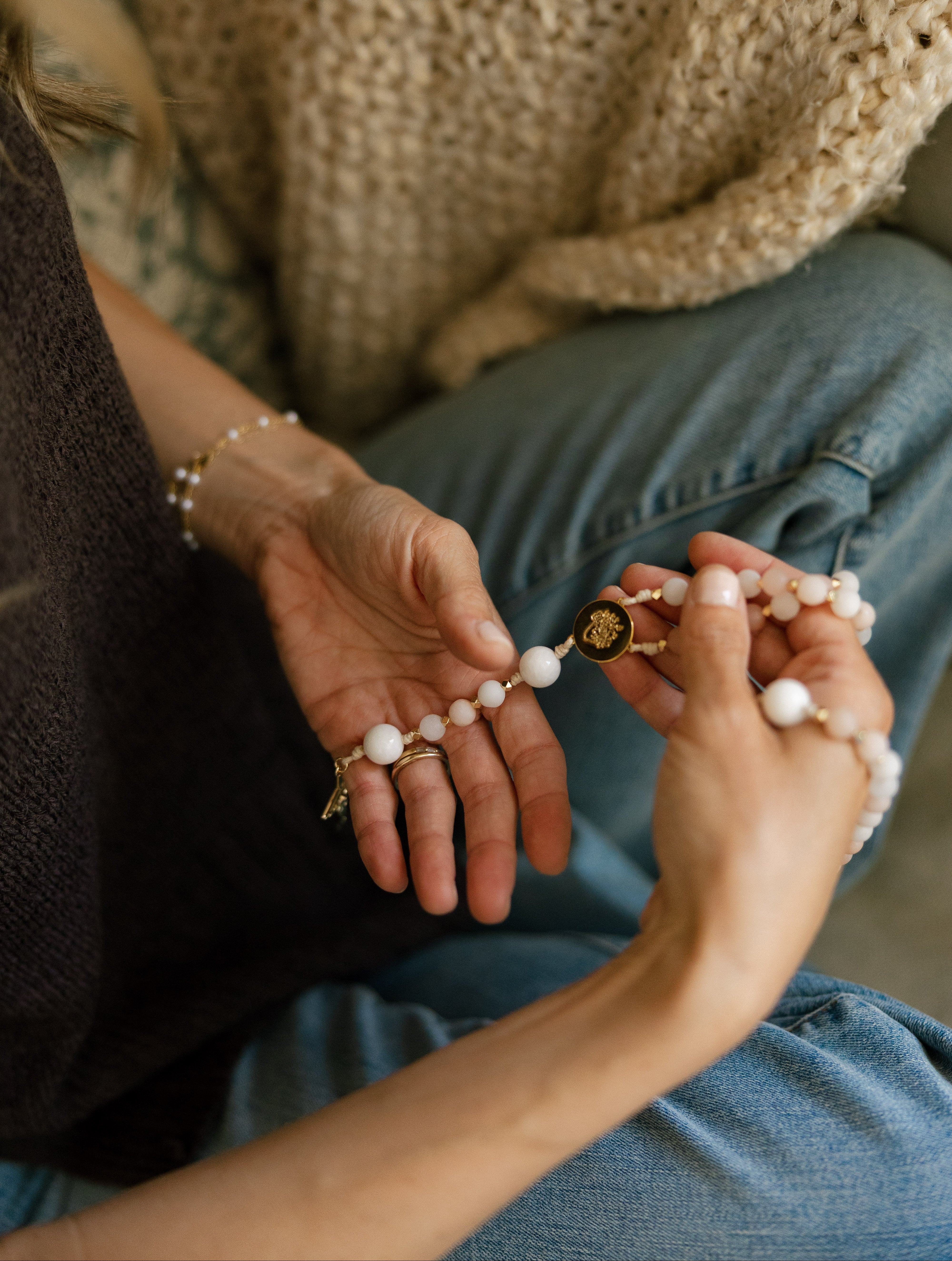 A close-up of a person's hands holding a pink and white beaded rosary with gold accents and an Immaculate Heart centerpiece.
